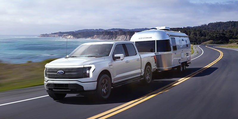white Ford F-150 Lightning running with towing at back